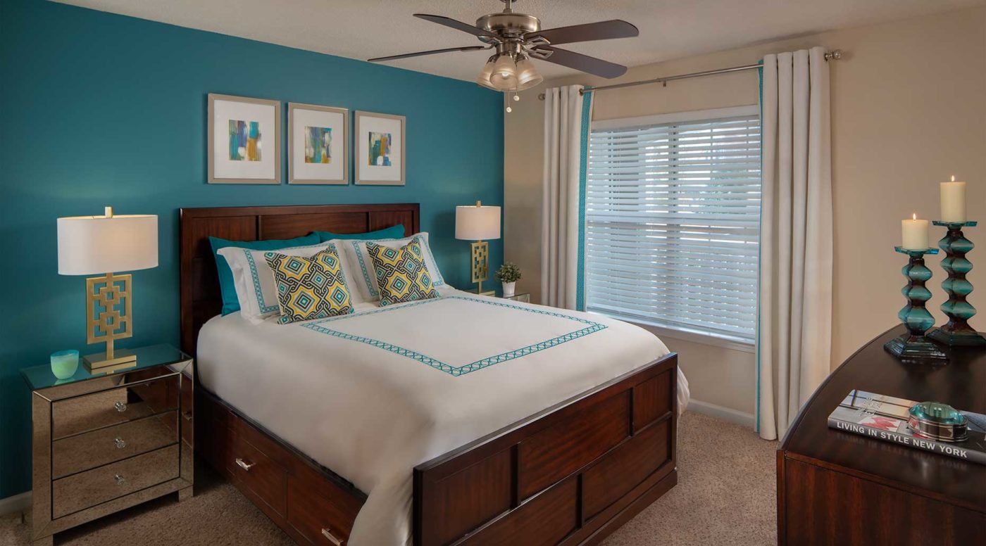 bedroom with ceiling fan, large window, teal accent wall, and dark wood furniture